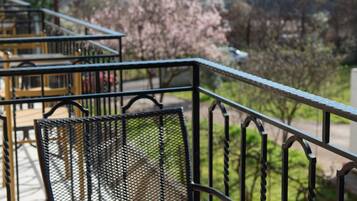 Un balcón con una mesa preparada para tomar té, con vistas a un paisaje montañoso y árboles en flor.
