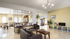 Amplia sala de estar con sofá, mesa de centro y televisor sobre un mueble. Se observa un comedor con muebles de madera y un ventanal grande.