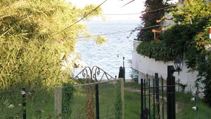 Vista costera con una reja de metal, vegetación y un edificio blanco.