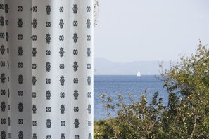 A coastal view with a sailboat on the water, a curtain with a geometric pattern, and greenery in the foreground. - Vontzos (Skiathos)