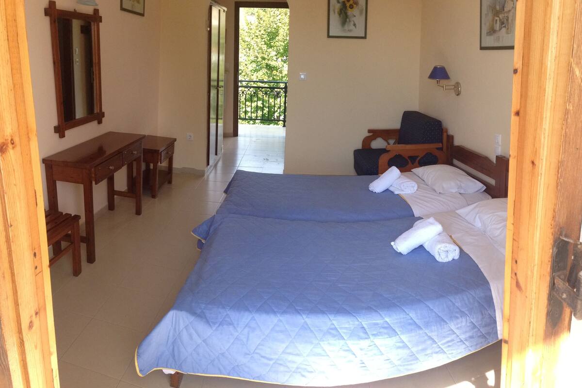 A room with two beds, a wooden desk, a chair, and a balcony.