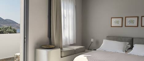 Une chambre à coucher moderne avec un grand lit, une table de chevet, une fenêtre avec des rideaux et des œuvres d’art encadrées accrochées au mur.