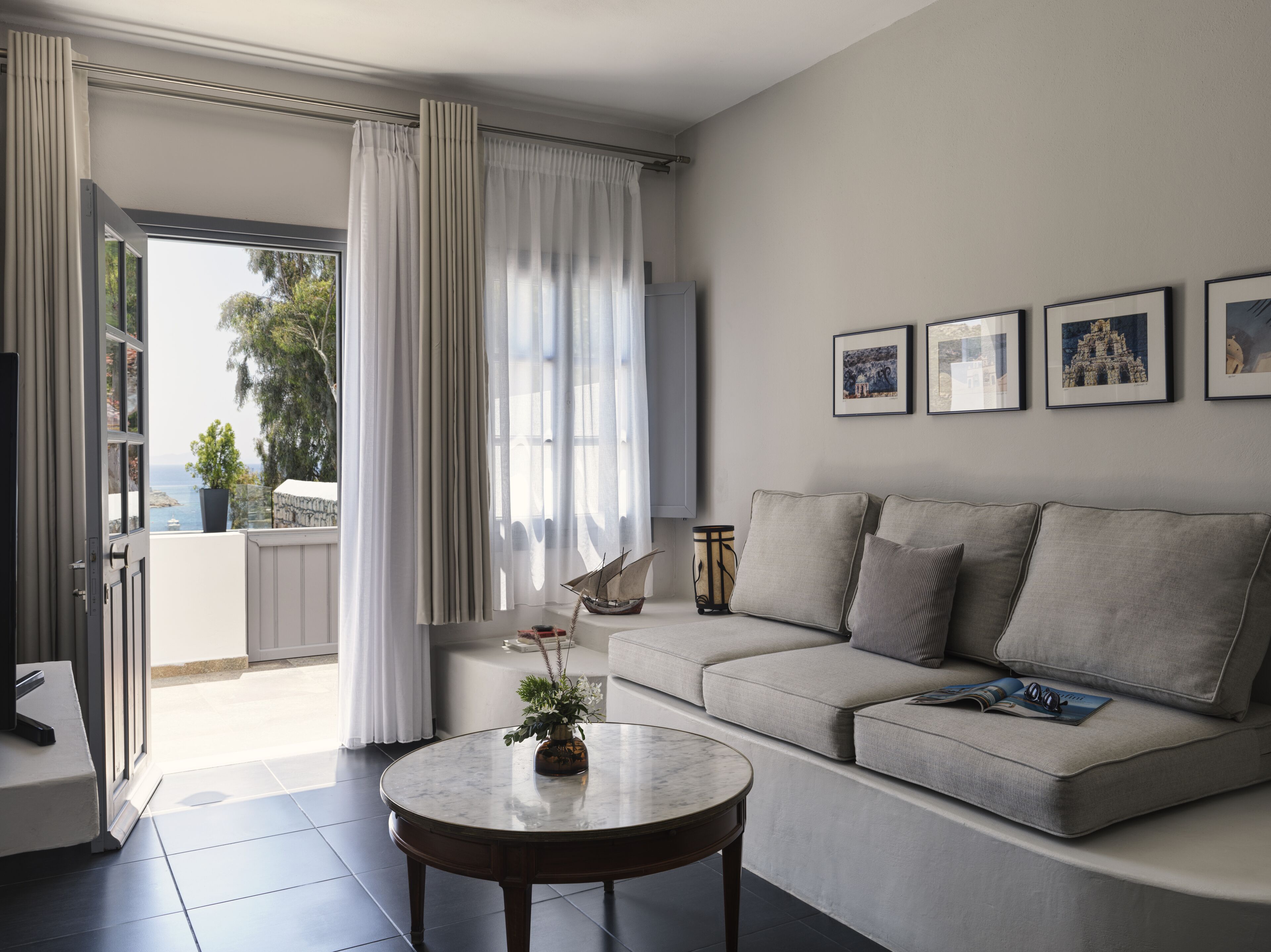 Una sala de estar moderna con un sofá gris, una mesa redonda de centro y vista al mar a través de amplios ventanales.