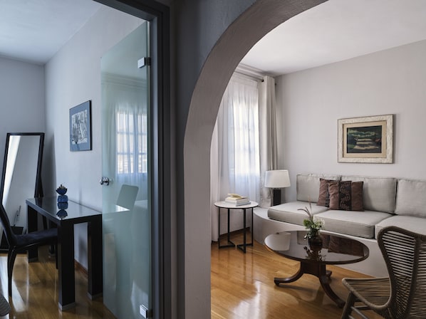 A modern living room with a glass door leading to a dining area, a sofa with cushions, a small round table with a lamp, and a framed picture on the wall. - The_Petra, Small Luxury Hotels of the World (Patmos)