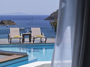 A poolside area with two lounge chairs and a table, overlooking a body of water and distant land. - The_Petra, Small Luxury Hotels of the World (Patmos)
