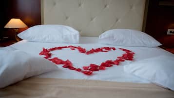 A bed with white linens and a heart-shaped arrangement of red rose petals.