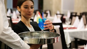 Una persona sosteniendo una bandeja con una bebida azul adornada con limón y una pajita.