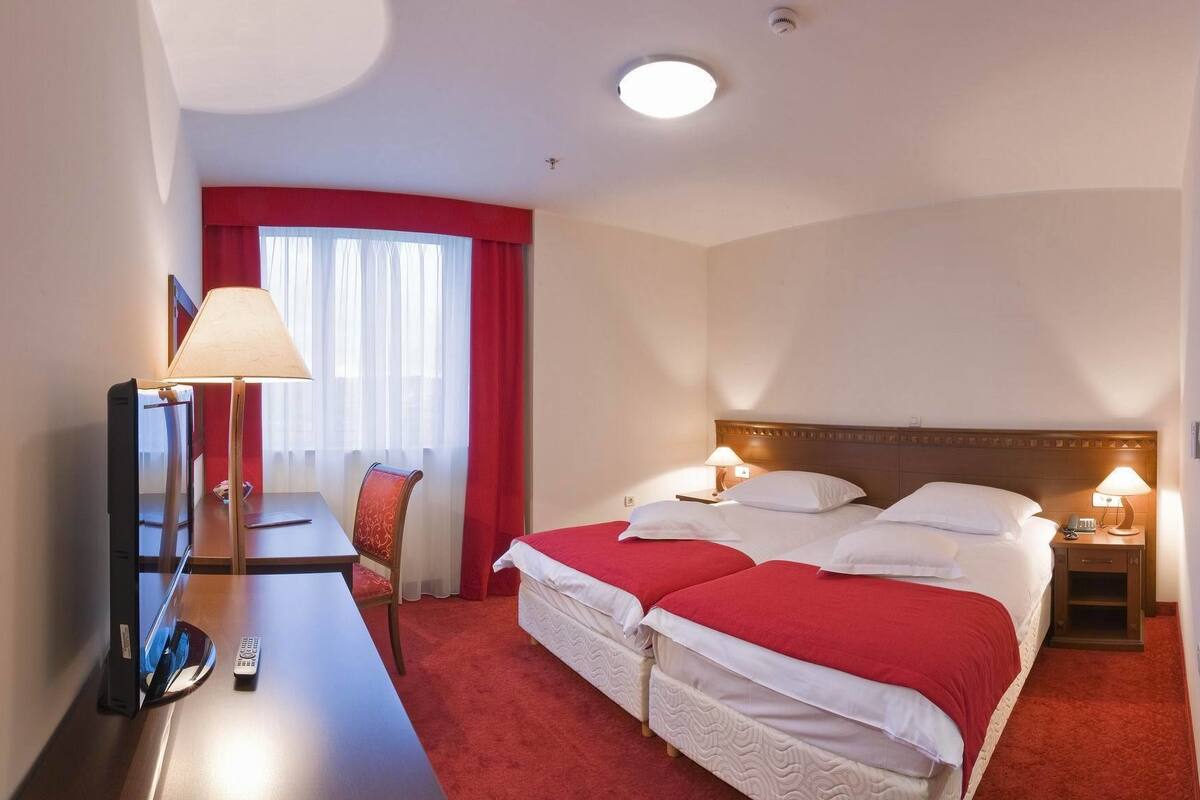 A hotel room with a large bed, a desk, a chair, a lamp, and a mirror.