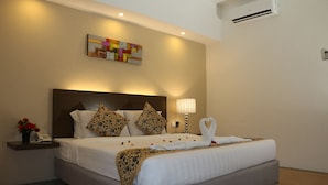 A hotel room with a large bed, a bedside table with a lamp, a wall-mounted air conditioner, and a colorful abstract painting. - Eagle Bay Hotel (Langkawi)