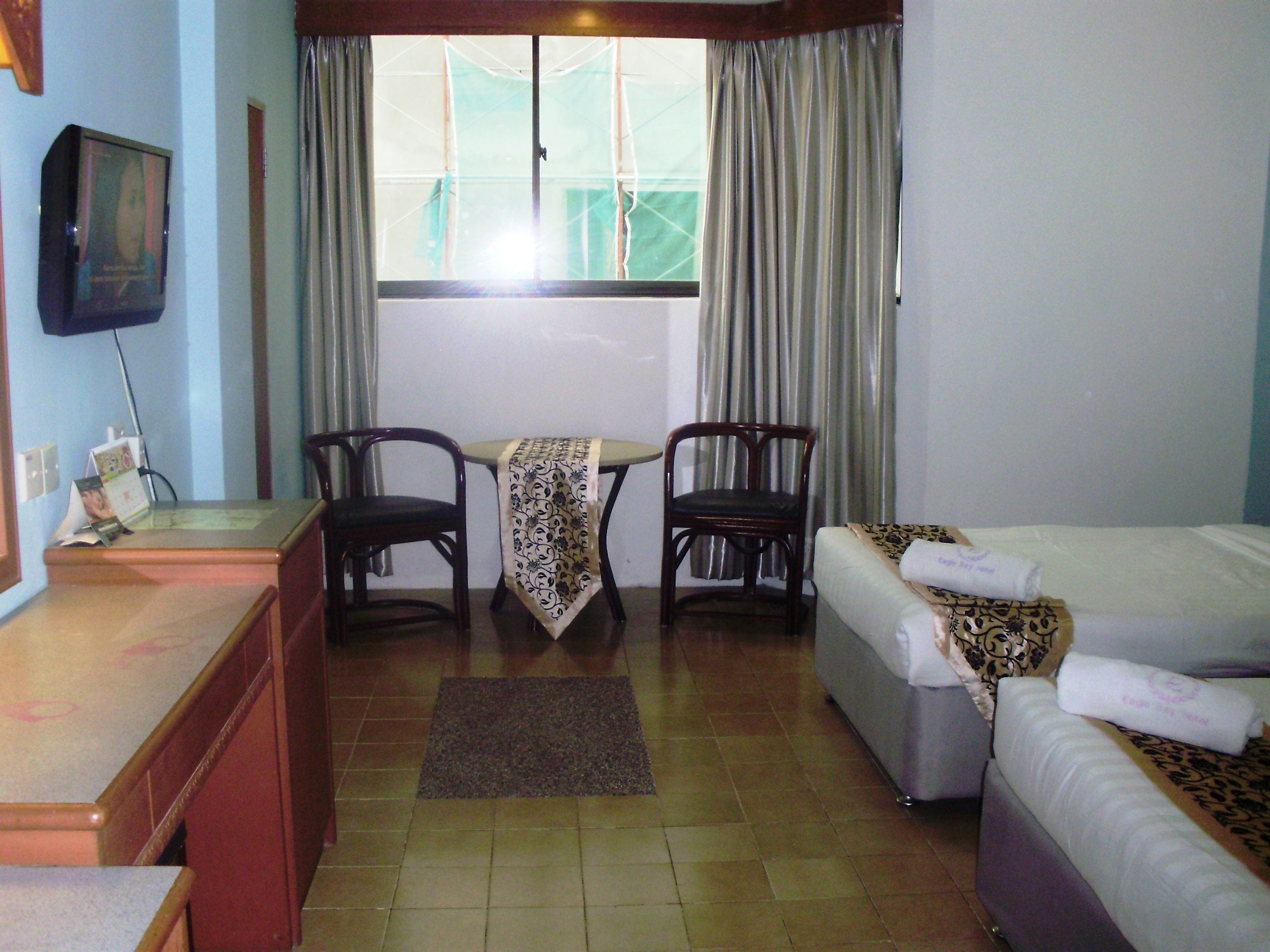 A hotel room with a bed, a desk, two chairs, a small table with a tablecloth, and a window with curtains.