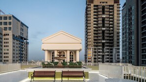 A rooftop terrace with a fountain, benches, and a view of surrounding high-rise buildings. - The Victory Executive Residences (Bangkok)