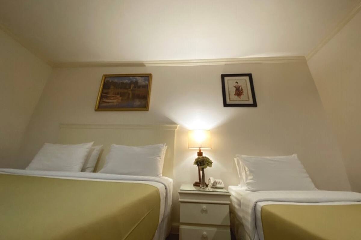 Ein Hotelzimmer mit zwei Einzelbetten, einem Nachttisch mit Lampe und zwei gerahmten Bildern an der Wand.
