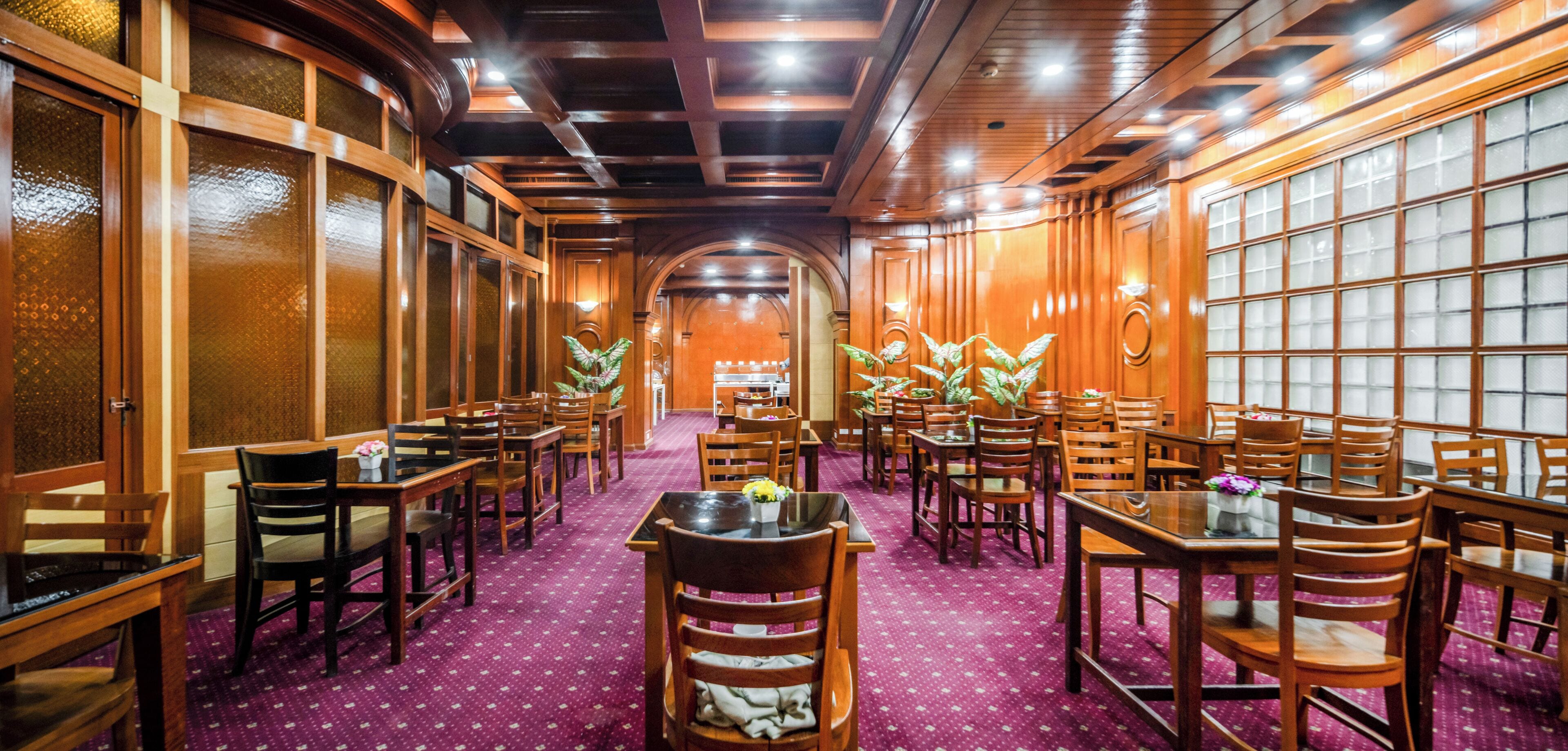 A restaurant with wooden tables and chairs, a purple carpet, and large windows with frosted glass panels.