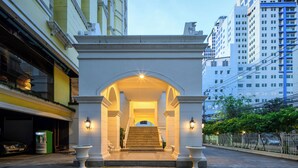 A grand entrance with a staircase leading to a covered area, flanked by columns and illuminated by wall sconces. - The Victory Executive Residences (Bangkok)