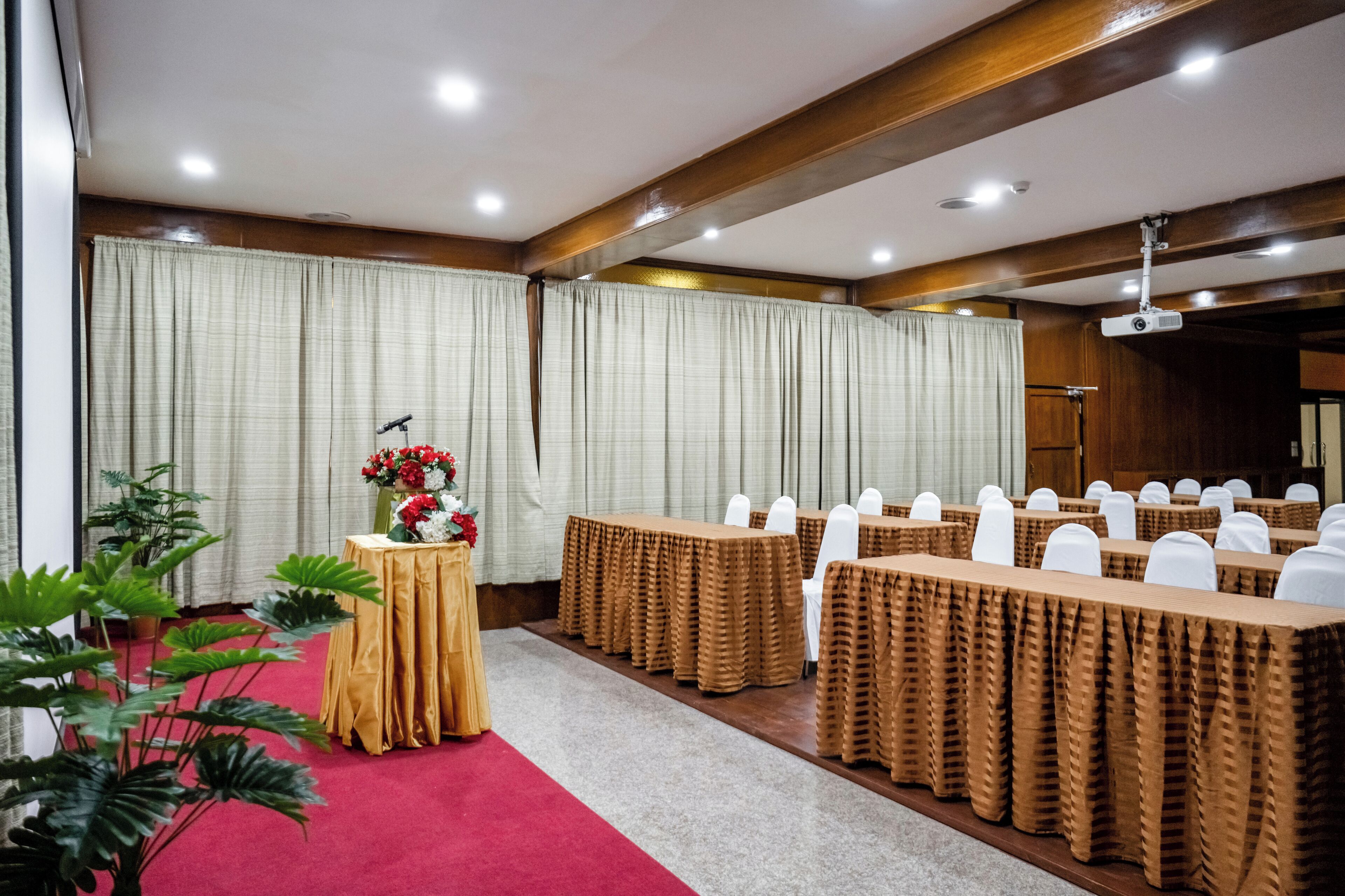 Een congreszaal met tafels bedekt met bruine tafelkleden, witte stoelen en een spreekgestoelte met een microfoon.