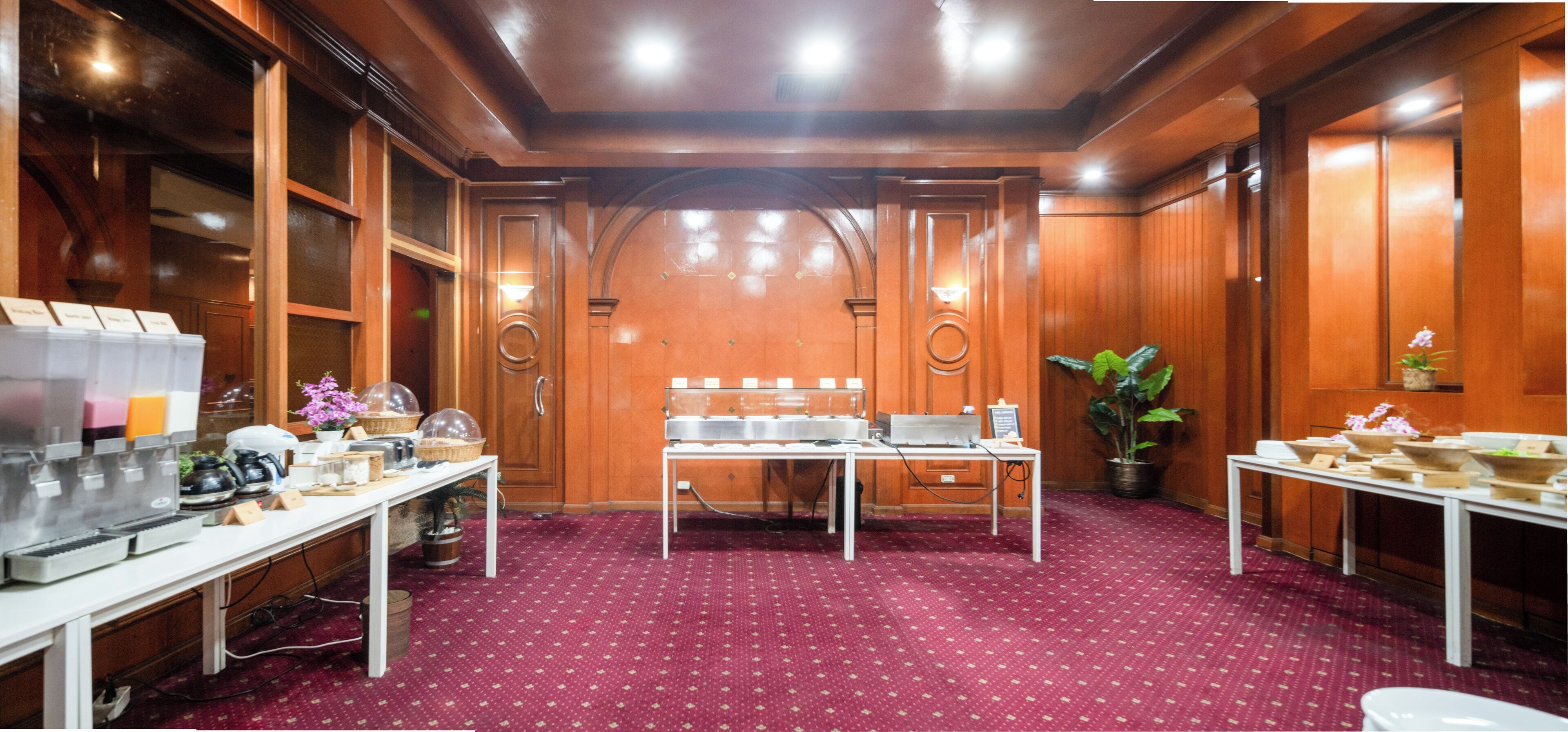 Une salle de conférence avec des panneaux de bois, une moquette rouge à motifs et des tables sur lesquelles se trouvent divers objets, notamment un ordinateur portable, une plante et une petite orchidée en pot.