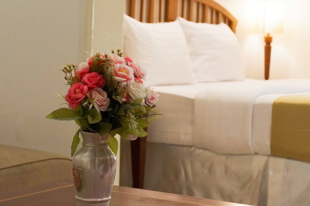 Ein Hotelzimmer mit einem Bett, einem Nachttisch mit Blumen und einer Nachttischlampe.
