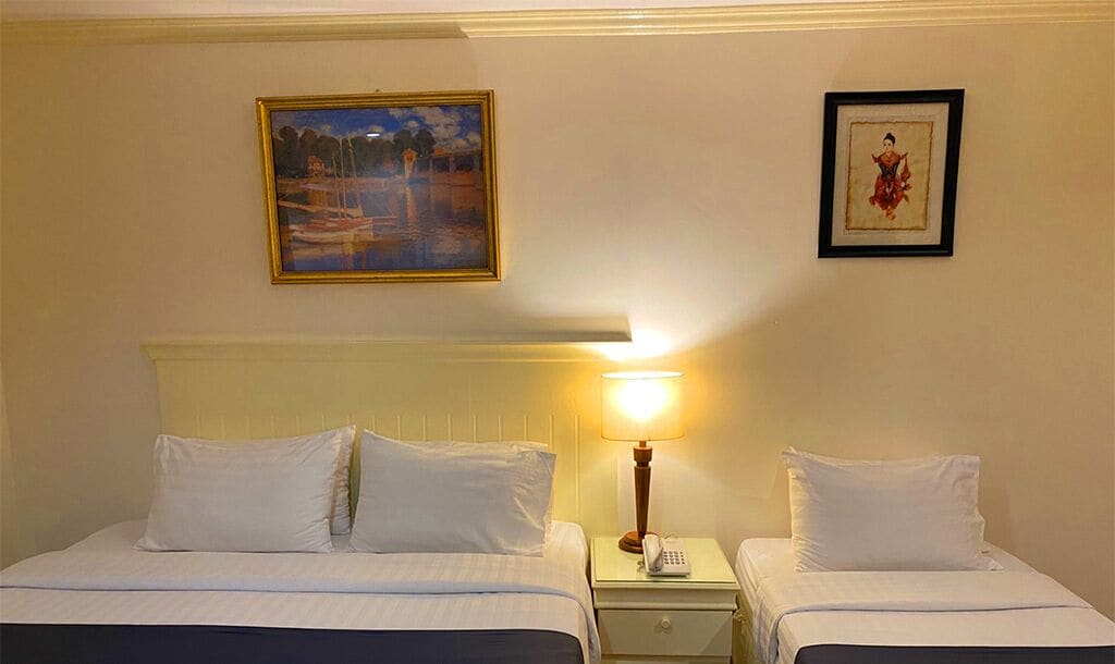 A hotel room with two beds, a nightstand with a lamp, and two framed pictures on the wall.