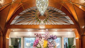 A lobby with a high ceiling, a chandelier, and a floral arrangement on a table. - The Victory Executive Residences (Bangkok)