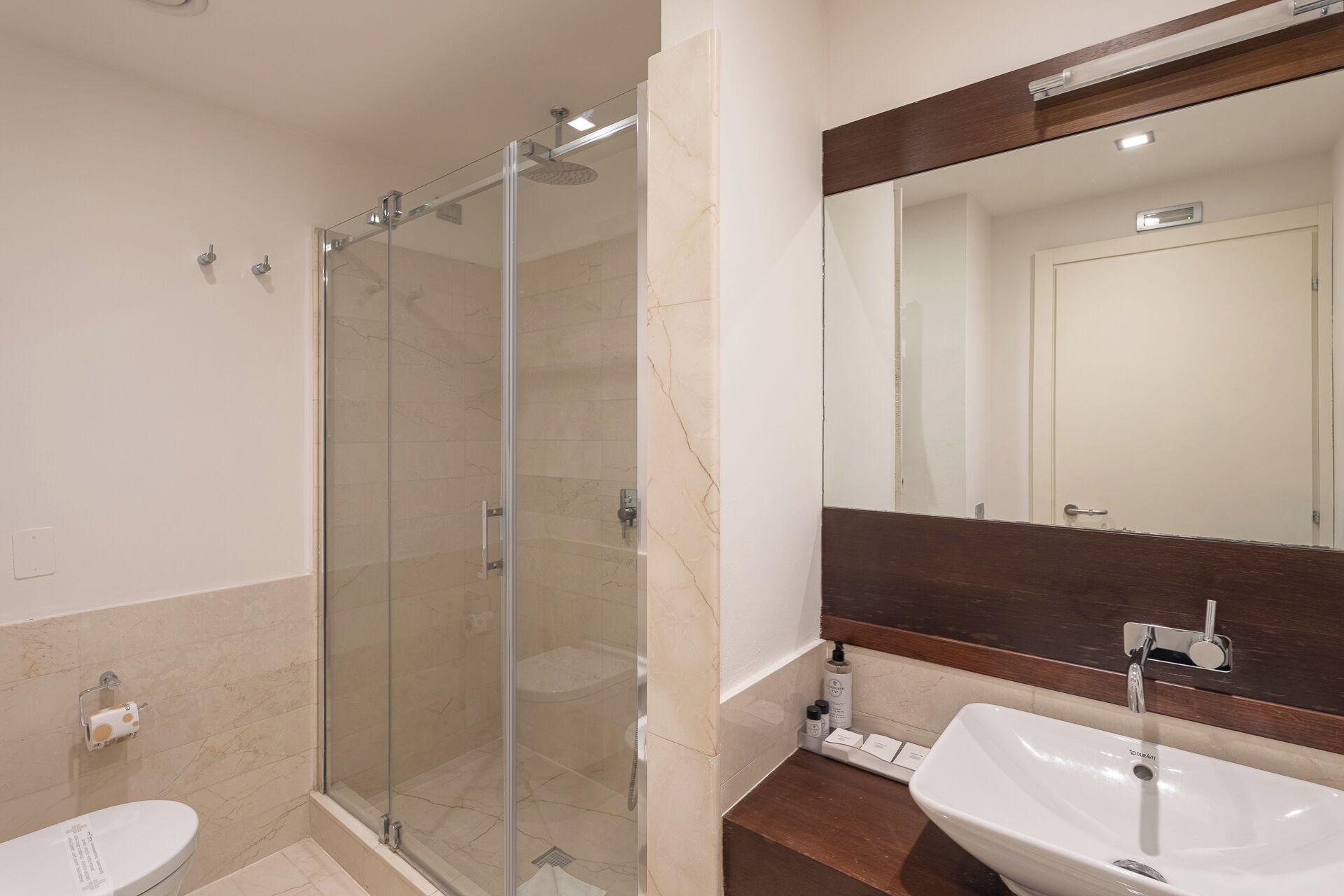 Un baño con ducha de vidrio, lavabo blanco y espejo sobre el lavabo.