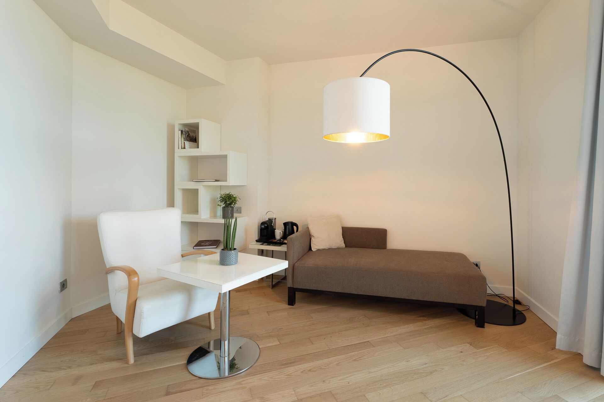 Ein modernes Zimmer mit einem weißen Schreibtisch, einem braunen Sofa, einem weißen Stuhl, einer Stehlampe und einem Bücherregal.