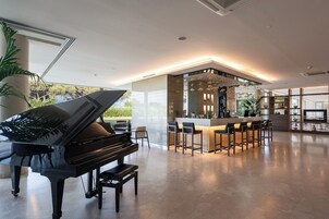 Un interior moderno con un piano de cola, una zona de bar y vistas al exterior con vegetación.
