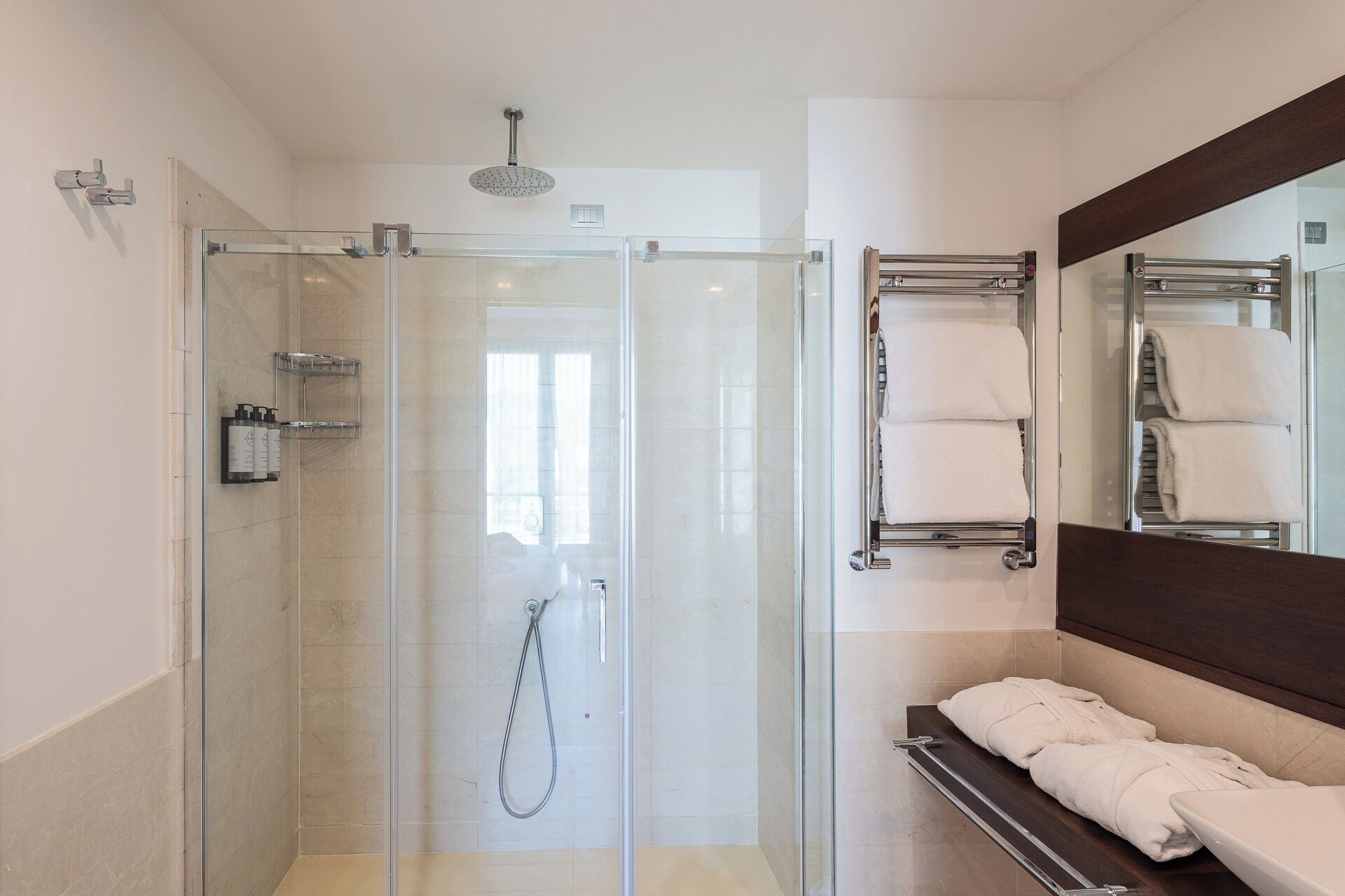 A modern bathroom with a glass-enclosed shower, a built-in towel rack, and a large mirror.