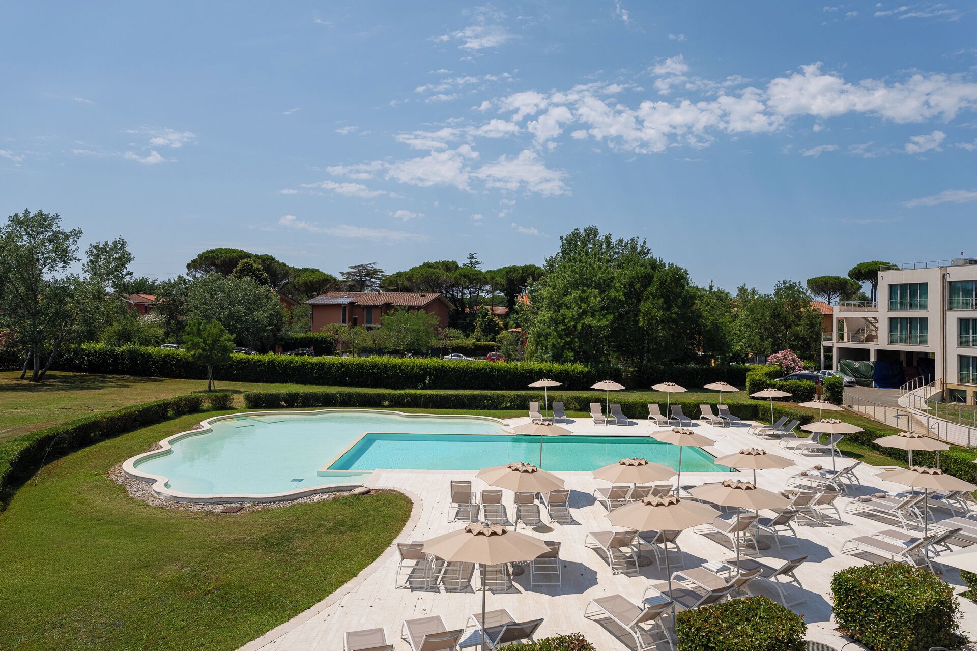 A swimming pool with lounge chairs and umbrellas, surrounded by greenery and buildings.