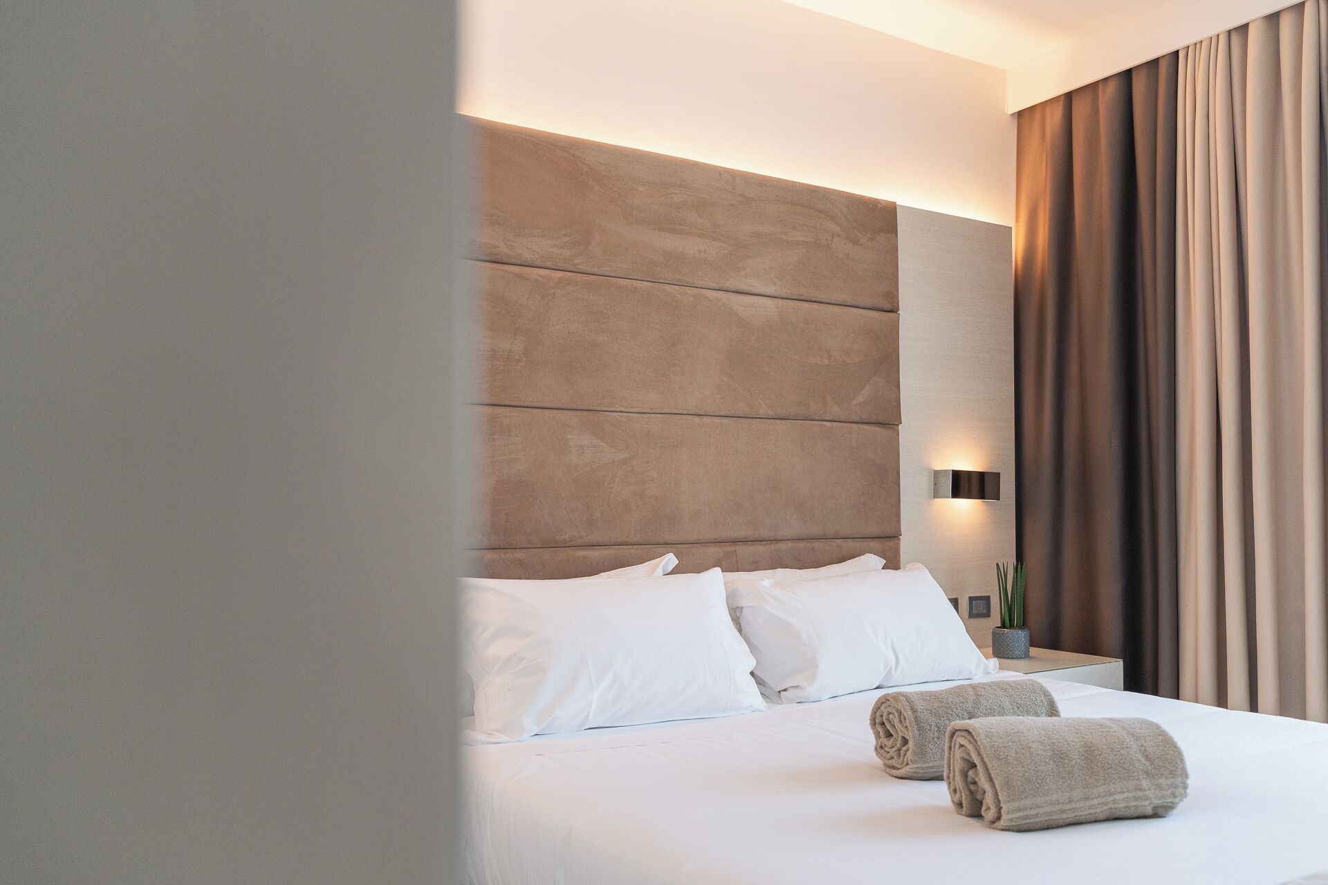 A hotel room with a large bed, white bedding, a headboard, and a nightstand with a lamp.