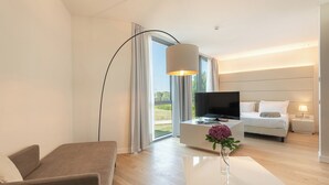 A modern hotel room with a sofa, a coffee table with a vase, a TV, a bed, and a large window. - Smy Pisa Plaza (Pisa)
