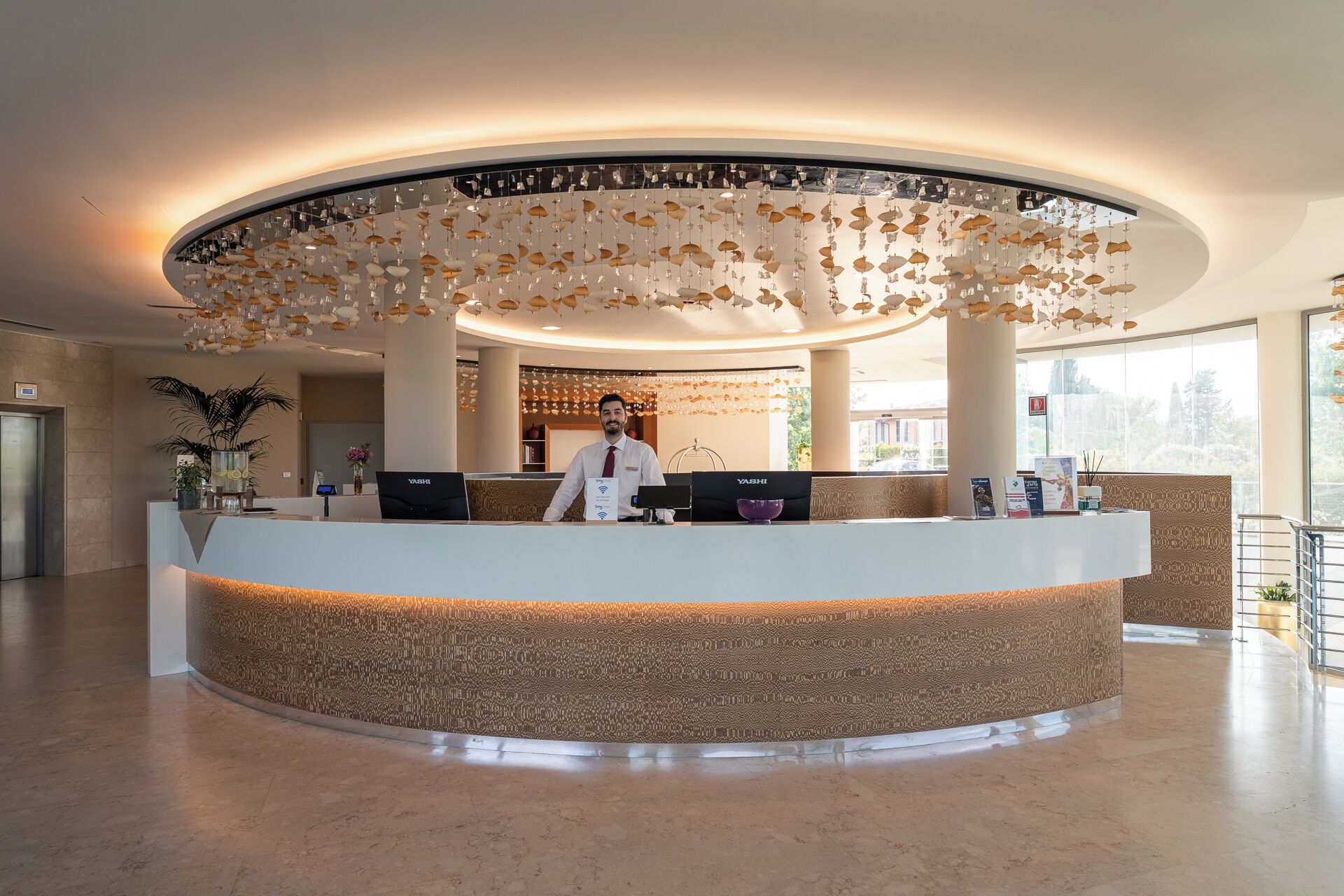 A reception area with a circular desk, a receptionist, and a ceiling with hanging light fixtures.