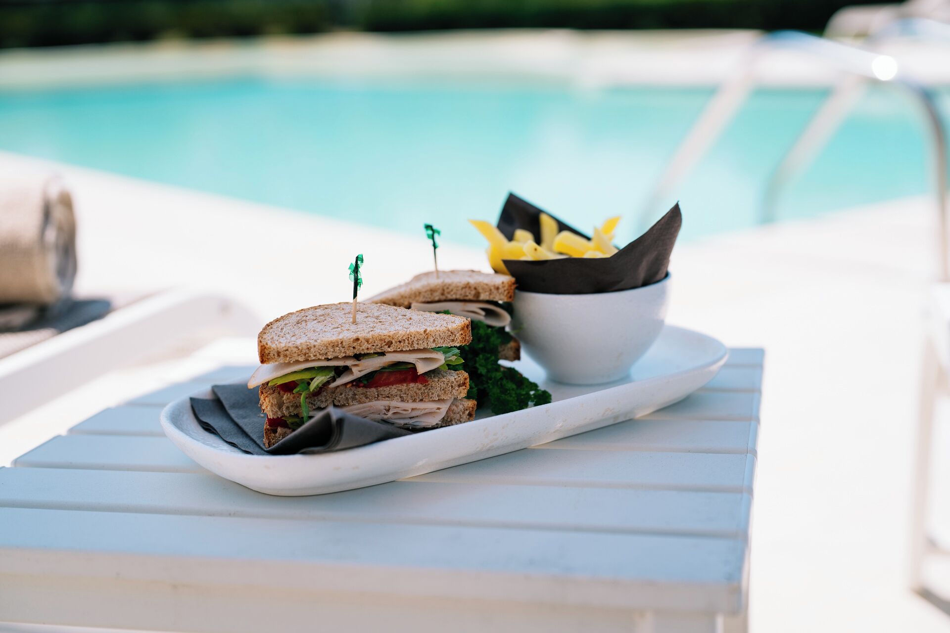 Un panino su un vassoio bianco, con una piscina sullo sfondo.