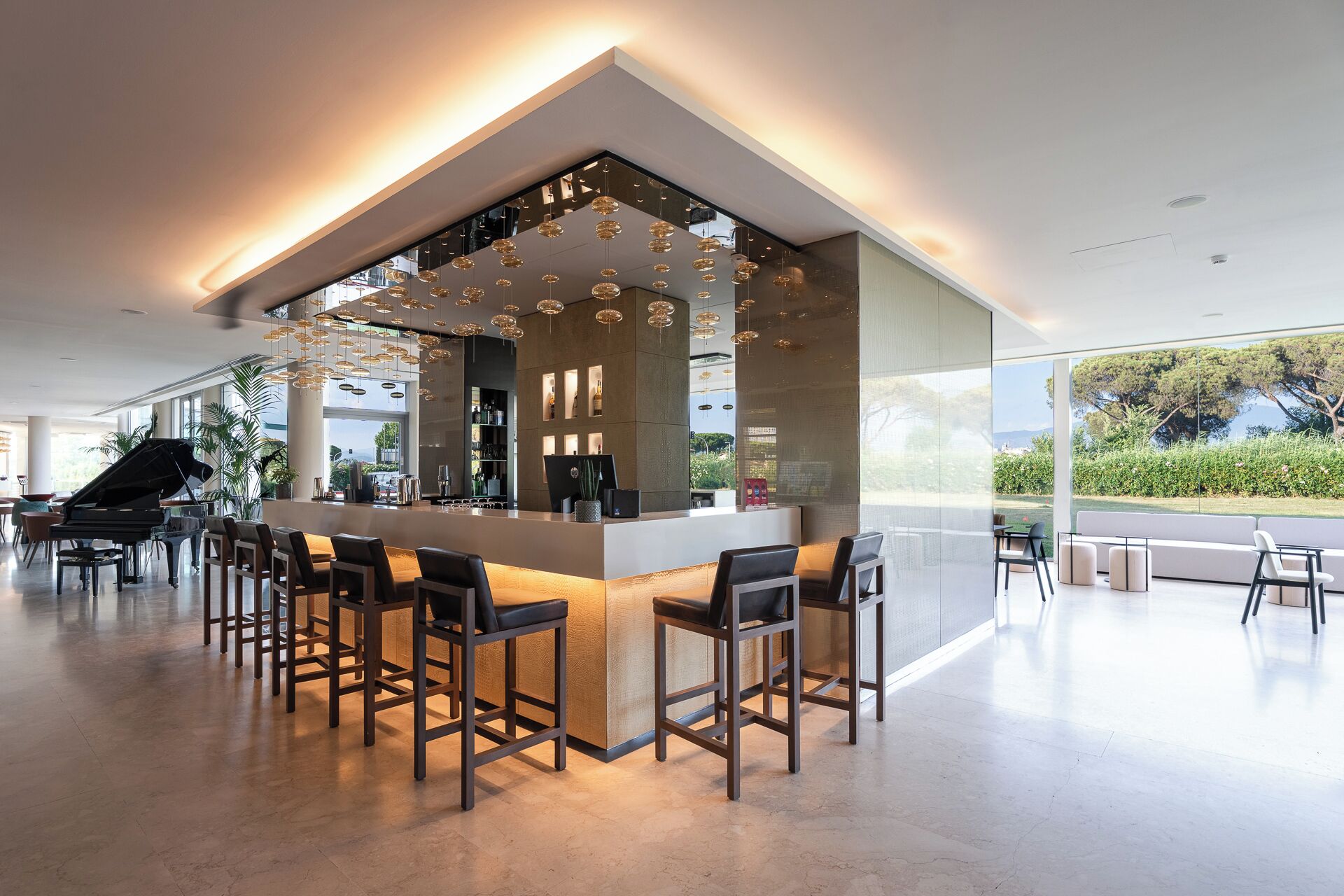 Een moderne bar met een piano, barstoelen en uitzicht op groen.