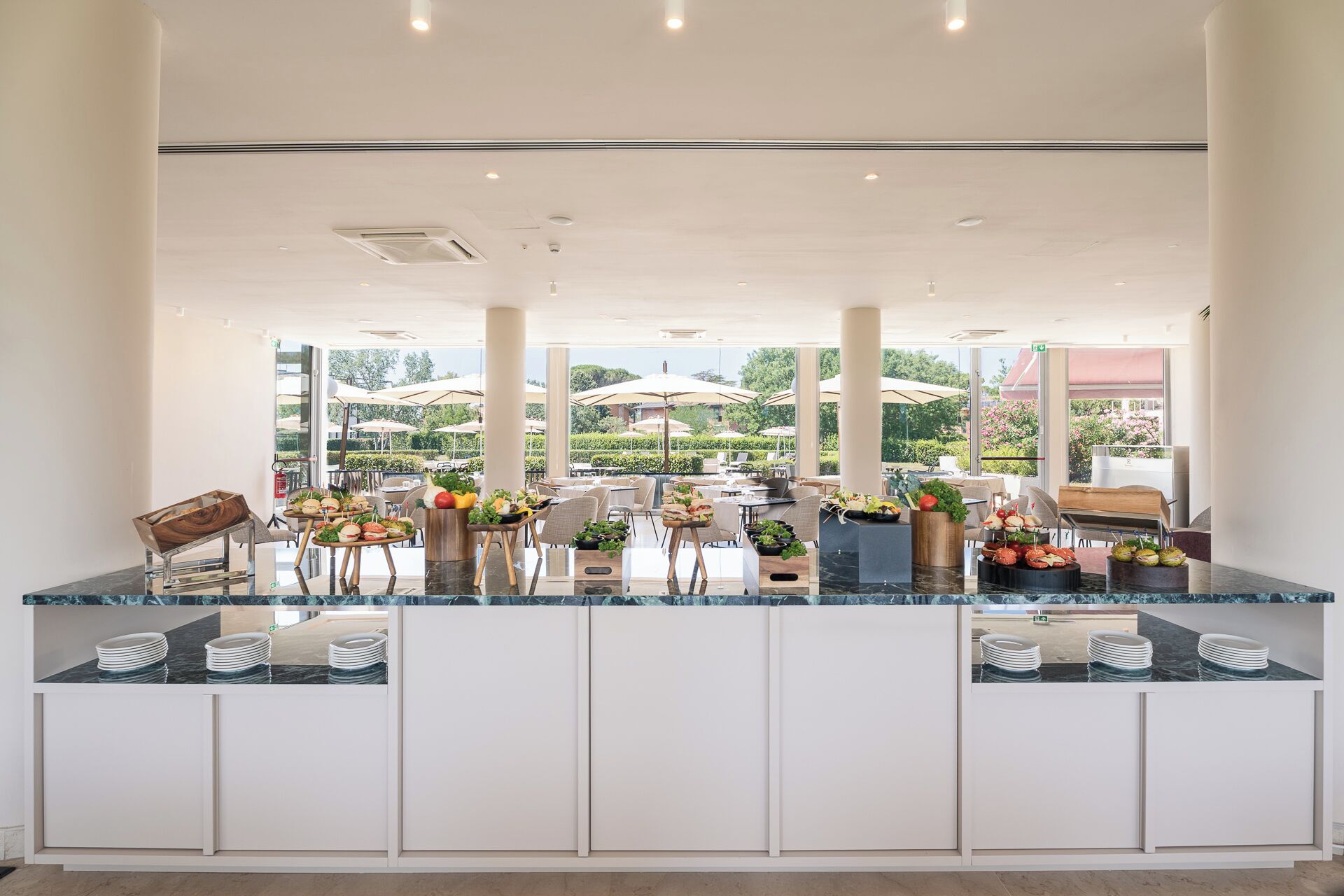 A modern outdoor dining area with a glass counter, white cabinets, and umbrellas.