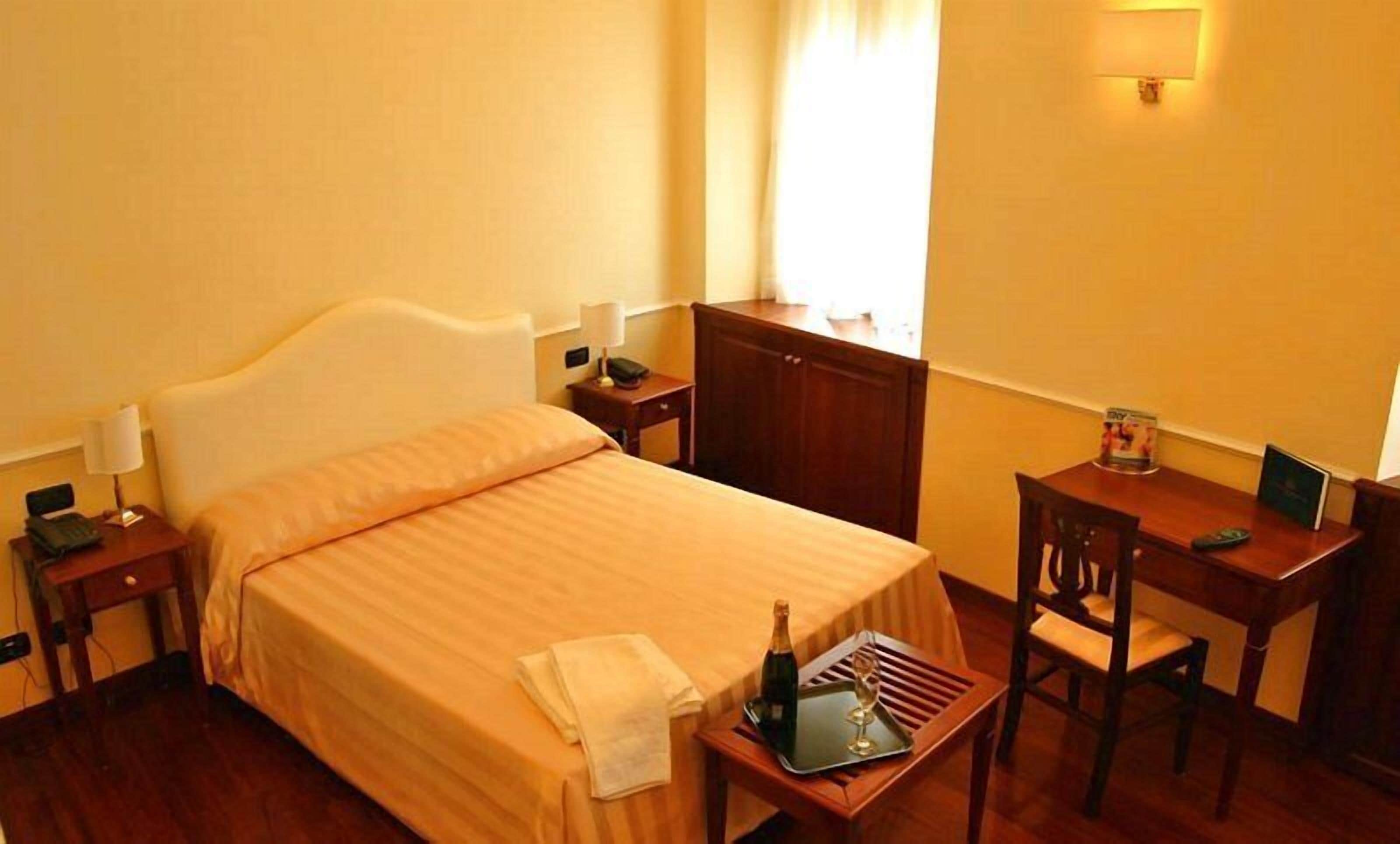 A hotel room with a bed, a desk, a chair, a bottle of champagne, and a tray.