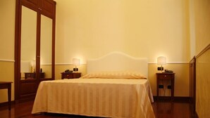 Una cama bien hecha con cabecera, dos mesitas de noche con lámparas, suelo de madera y un espejo grande en la pared.