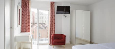 A hotel room with a bed, a desk, a chair, a wardrobe, and a TV.