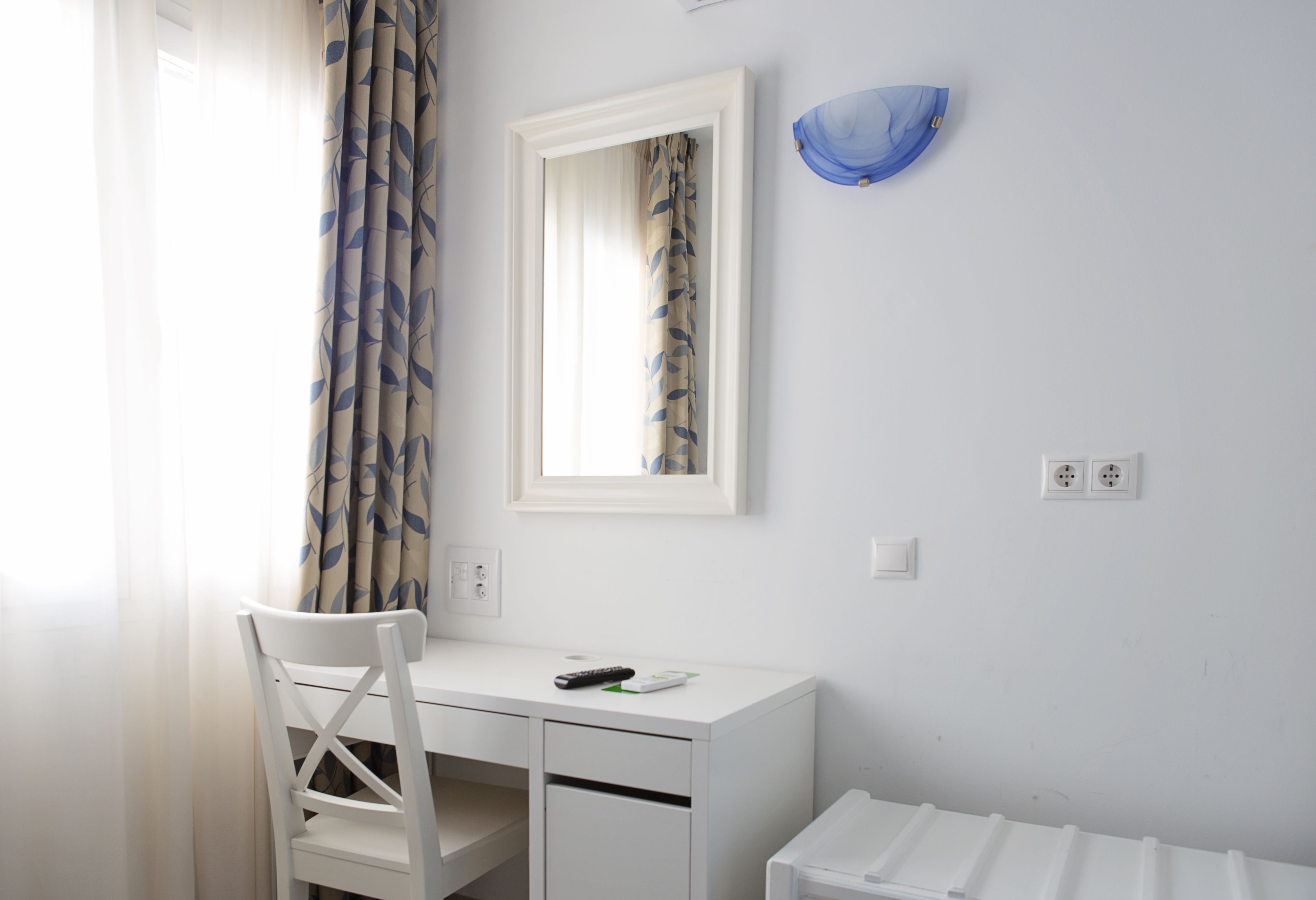 A white desk with a chair, a mirror, and a remote control.