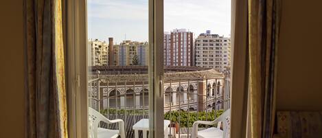 Un balcón con sillas y una mesa de plástico blanco, con vistas a un paisaje urbano que incluye edificios y un patio tradicional.