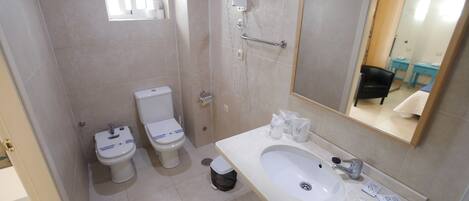 Une salle de bain avec deux toilettes, un lavabo, une douche et un miroir.