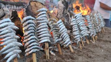 Pescado ensartado en palos de madera sobre fuego abierto.