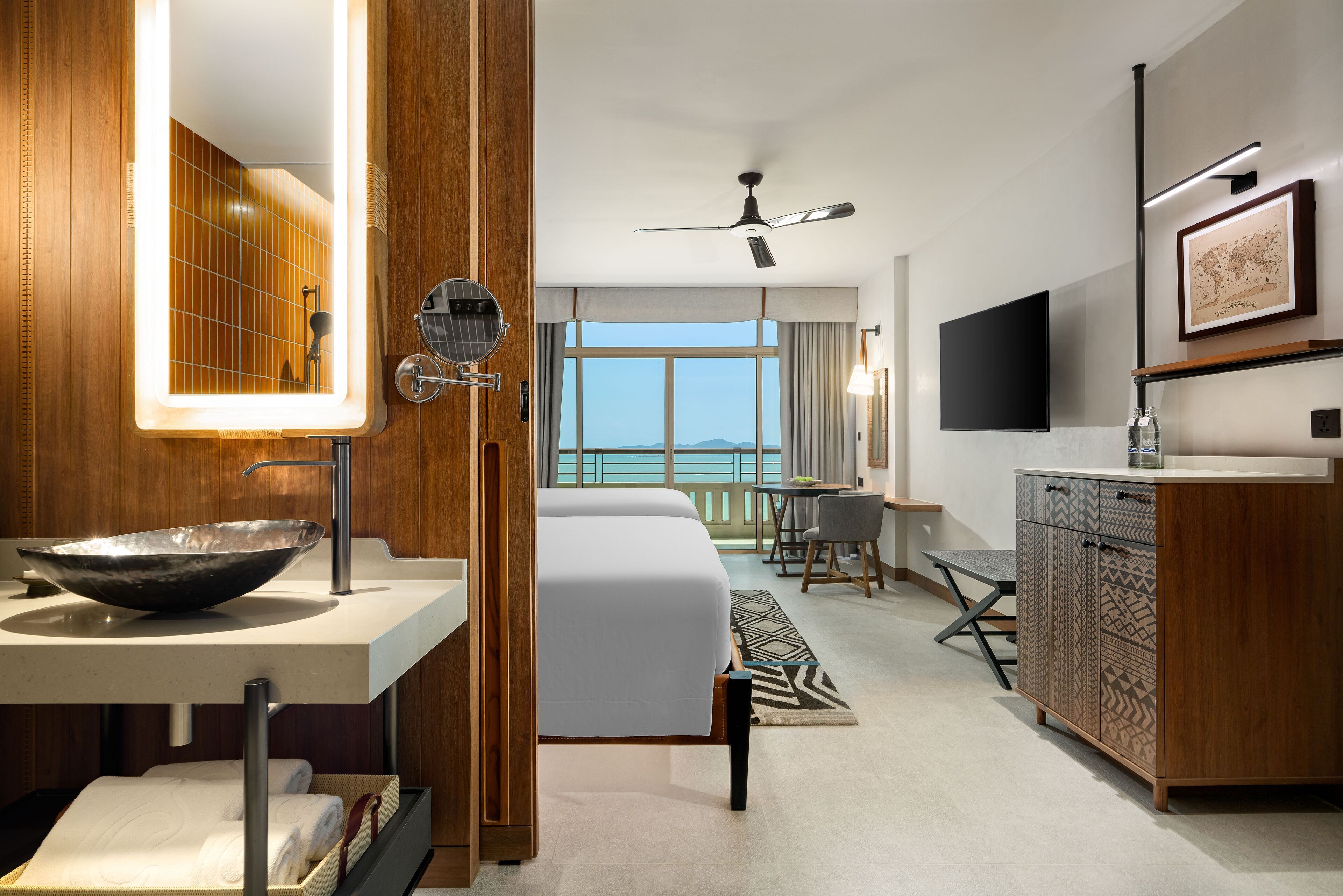 Una habitación de hotel moderna con un ventanal grande, una cama, un baño con un espejo amplio, un lavamanos y un armario.