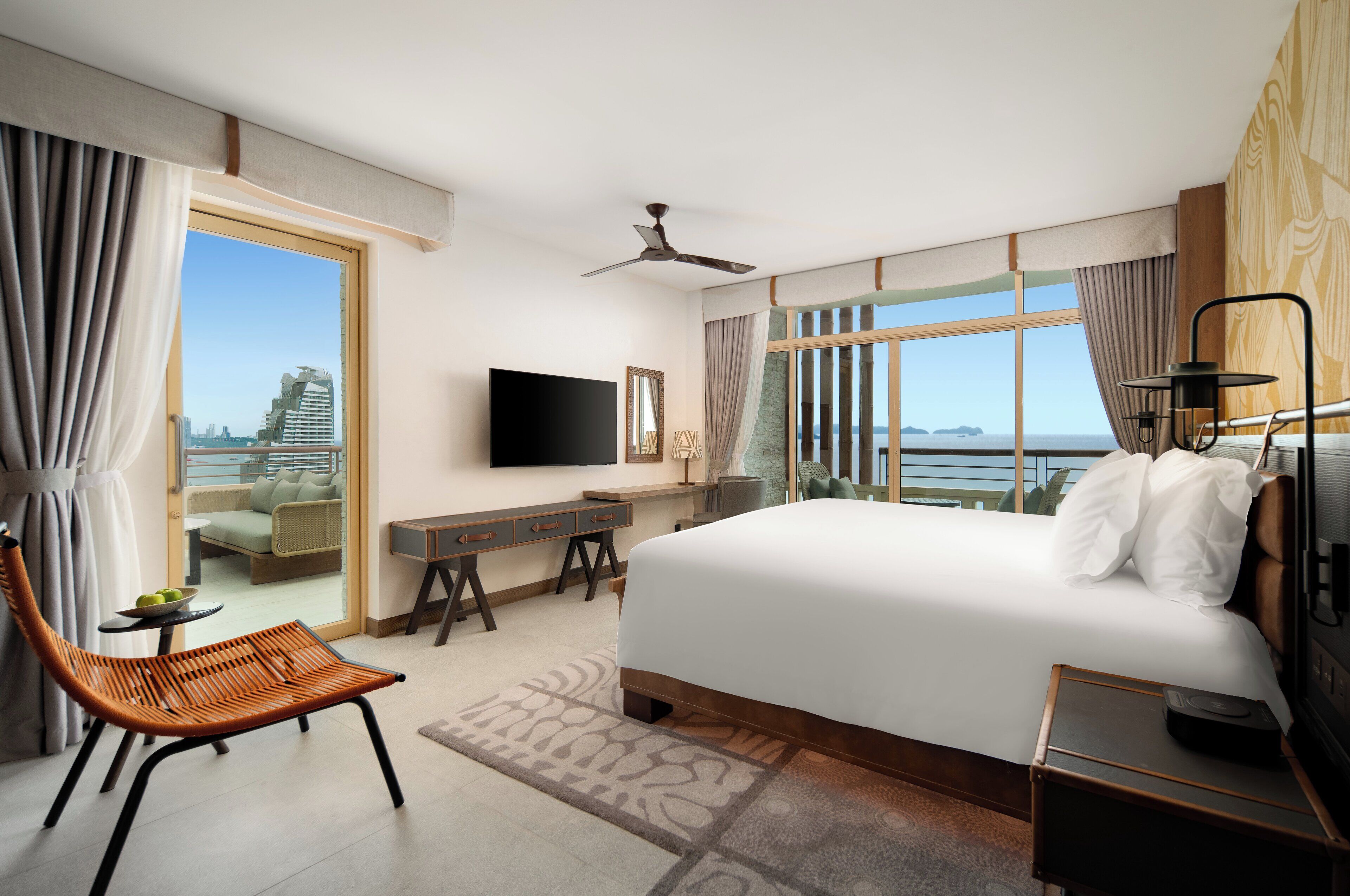 Habitación de hotel con cama, escritorio, silla, televisor y balcón con vistas.