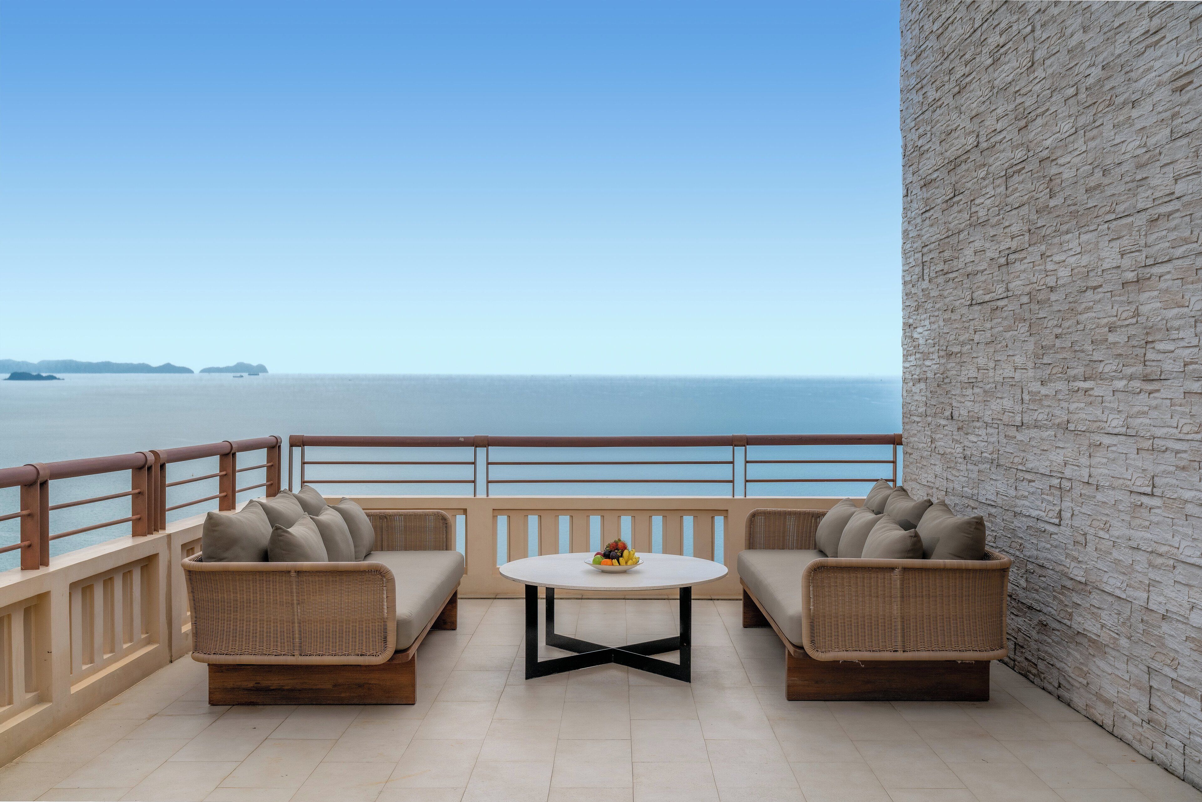 A balcony with wicker furniture and a table, overlooking a calm sea.
