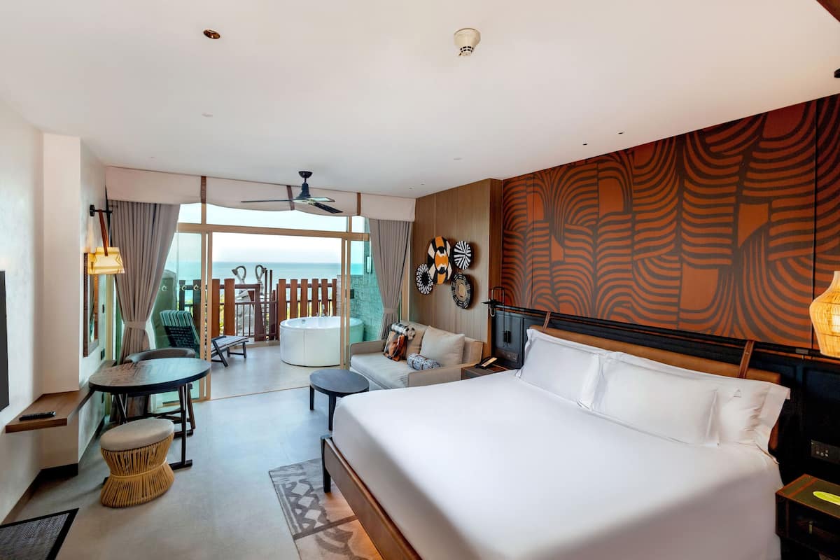 Habitación de hotel con una cama grande, balcón con vistas, zona de comedor y ventilador de techo.