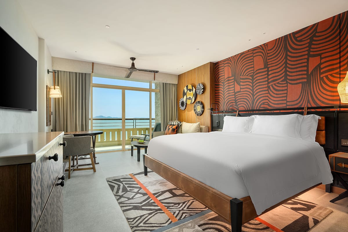 Habitación de hotel moderna con una cama grande, un escritorio, una silla y un balcón con vistas.