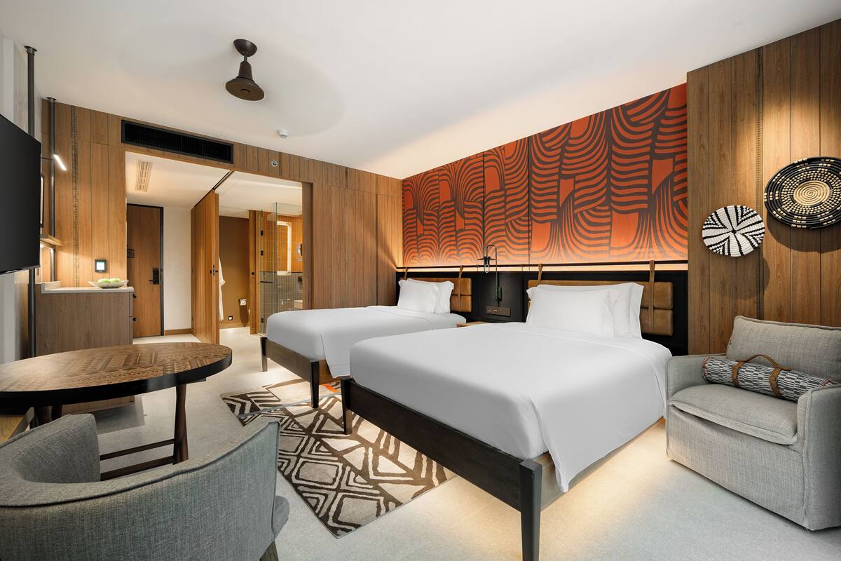 Una habitación de hotel moderna con dos camas, un sofá, una mesa de comedor y un panel decorativo en la pared.