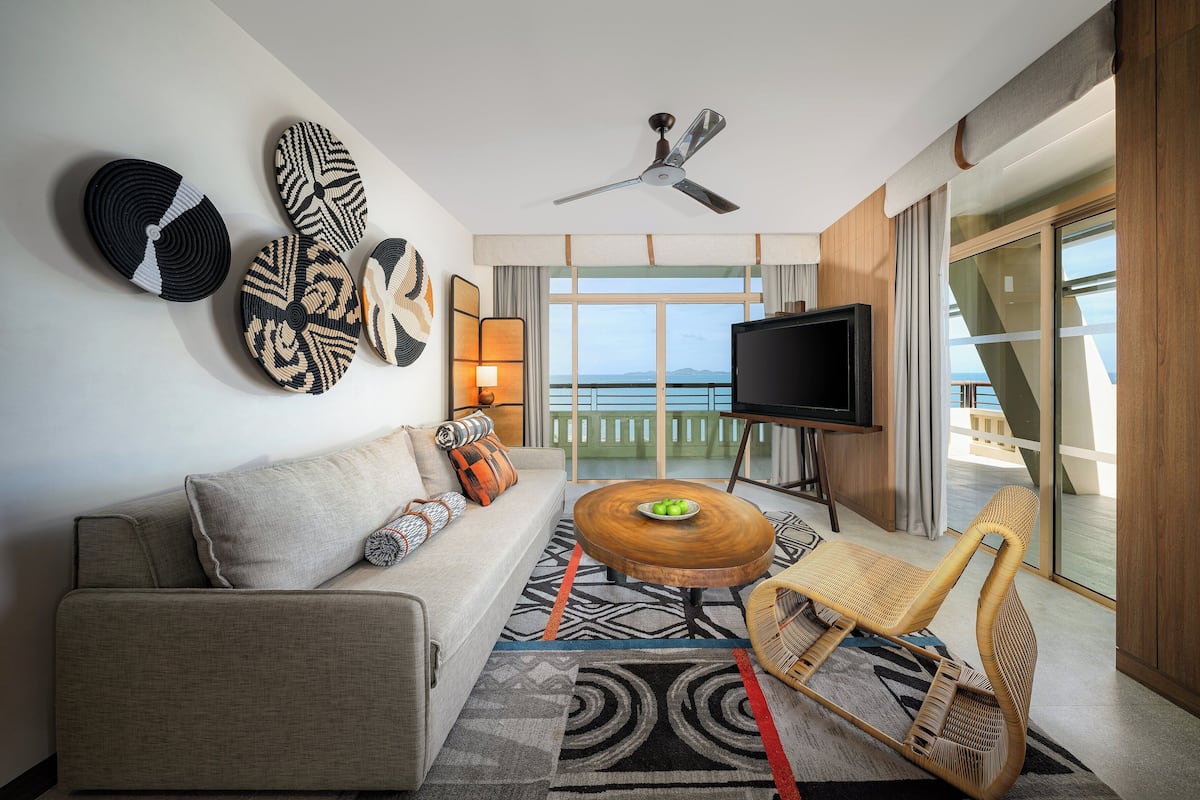 Una sala de estar moderna con un sofá, una mesa de centro y un televisor. Hay un balcón con vista al mar.