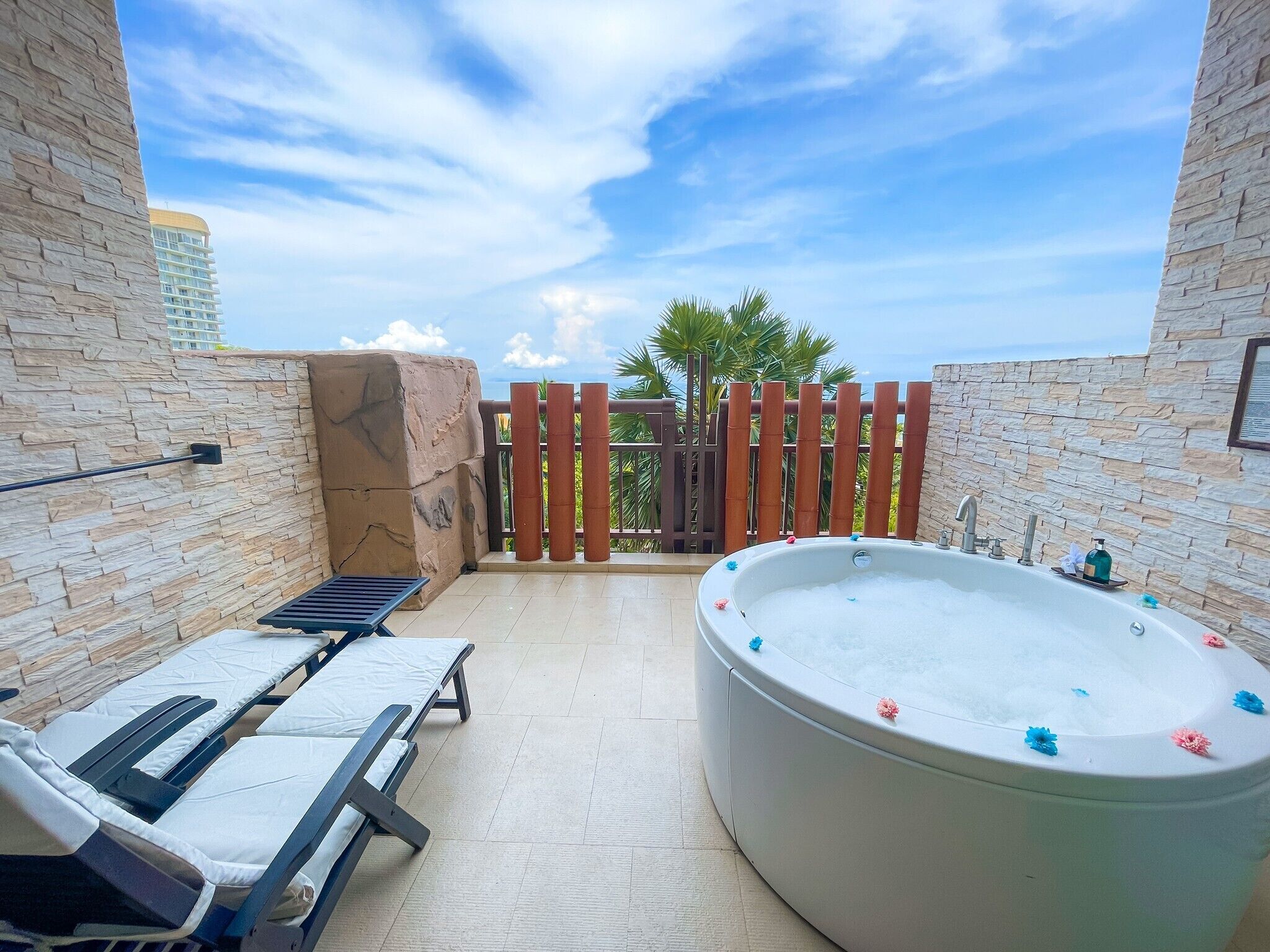 Une terrasse sur le toit avec un jacuzzi, des chaises longues et une vue sur les palmiers et les immeubles.
