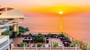 Terraza en la azotea con mobiliario exterior y vistas a la puesta de sol sobre el agua.
